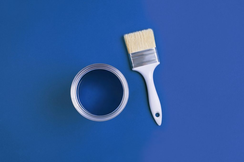 Paint brush with an open can of paint on trendy Classic Blue background.